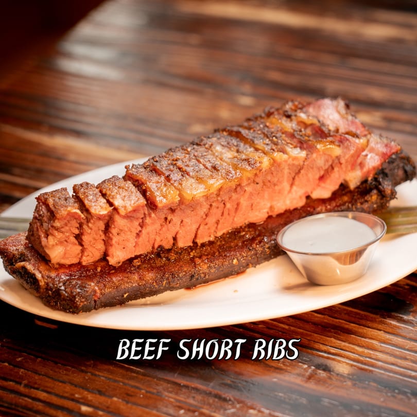 Succulent beef short ribs, sliced and served with a creamy white sauce on a wooden table.