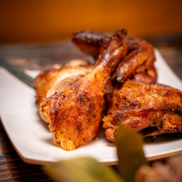 Close-up of golden-brown grilled chicken pieces on a white plate, showcasing crispy skin and juicy meat.