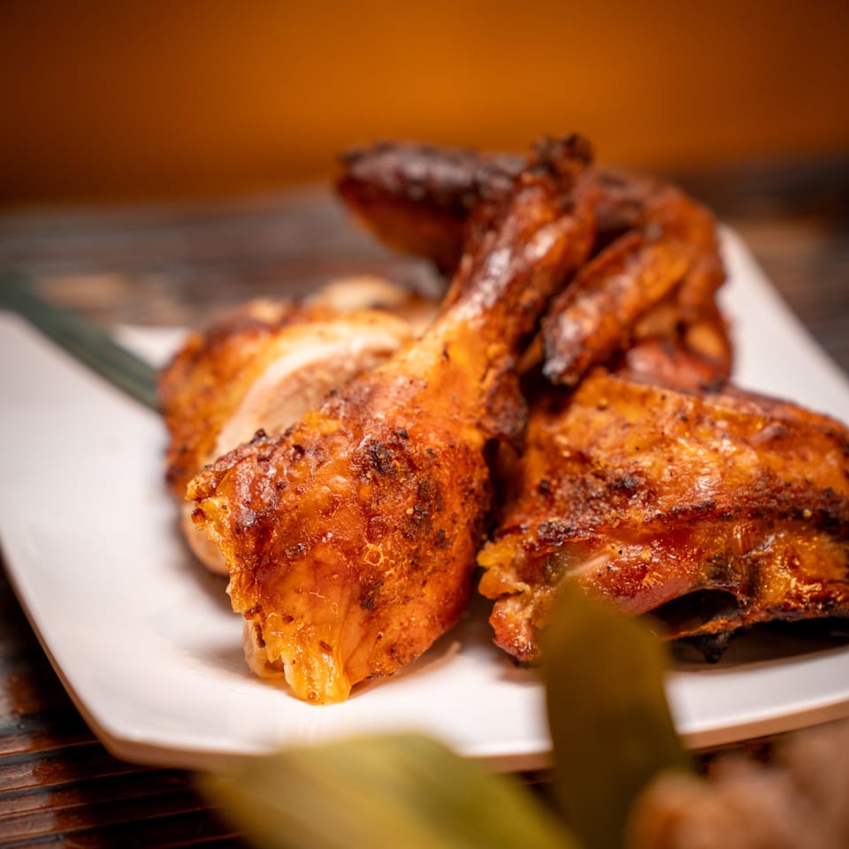 Close-up of golden-brown grilled chicken pieces on a white plate, showcasing crispy skin and juicy meat.