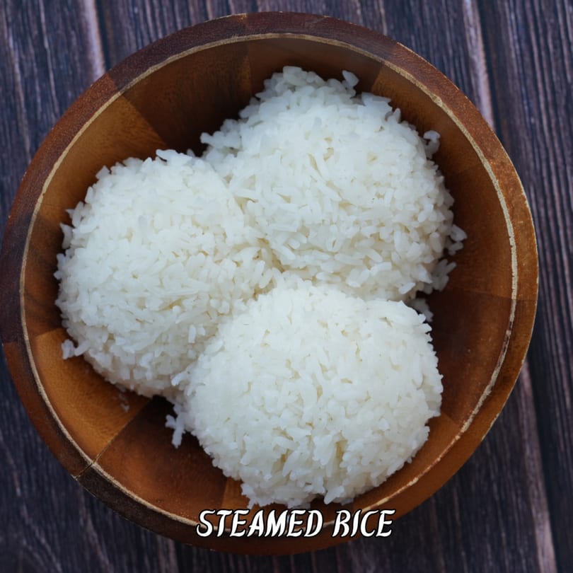 Three mounds of white steamed rice in a wooden bowl on a dark wooden table.