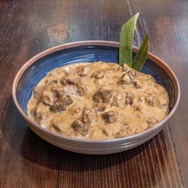 A blue bowl of Filipino Bicol Express, a creamy pork dish, garnished with green leaves on a wooden table.