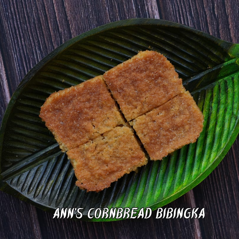 Four square pieces of golden-brown, sugar-dusted Ann's Cornbread Bibingka on a green leaf plate.