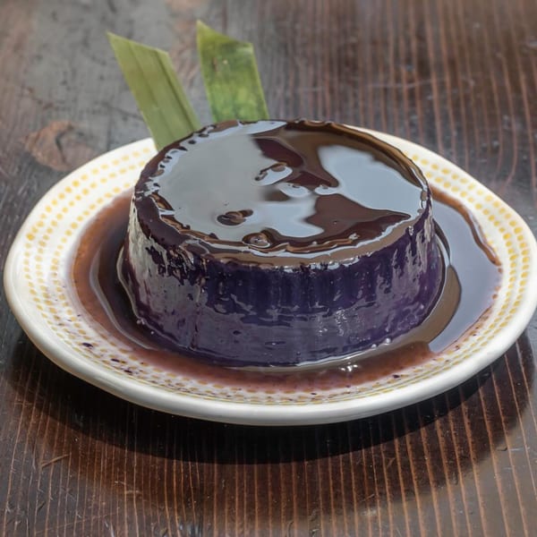Purple ube panna cotta with dark chocolate sauce and green garnish on a white plate.